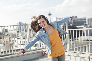 Germany, North Rhine-Westphalia, Cologne, portrait of smiling young woman with outstretched arms standing on parking level - FEXF000141