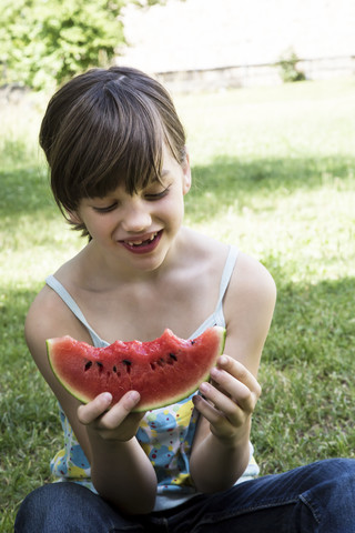 Lächelndes Mädchen isst ein Stück Wassermelone im Garten, lizenzfreies Stockfoto