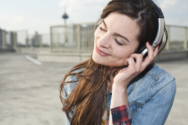 Germany, North Rhine-Westphalia, Cologne, portrait of smiling young woman listening music with headphones - FEXF000138