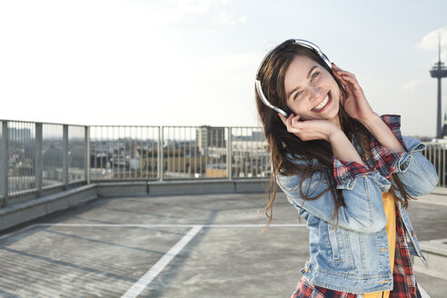 Deutschland, Nordrhein-Westfalen, Köln, Porträt einer lachenden jungen Frau, die mit Kopfhörern Musik hört - FEXF000139