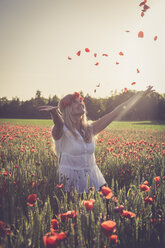 Woman jumping in a poppy field throwing petals in the air - SARF000718