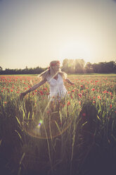 Woman dancing in a poppy field at back light - SARF000738