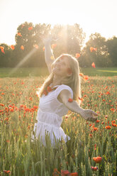 Woman standing in a poppy field throwing petals into the air - SARF000735