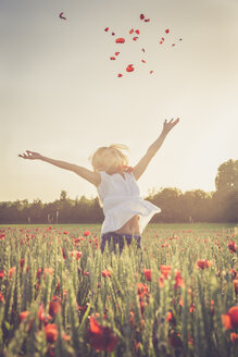 Woman jumping in a poppy field throwing petals in the air - SARF000736
