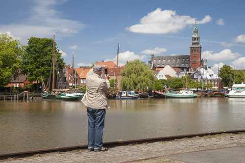 Deutschland, Niedersachsen, Leer, älterer Mann fotografiert mit seinem Smartphone die Stadt und den Museumshafen, lizenzfreies Stockfoto
