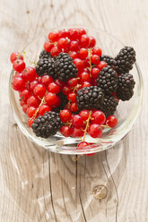 Glass bowl od red currants and blackberries on wooden table, elevated view - SARF000720