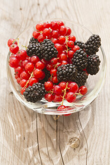 Glasschale mit roten Johannisbeeren und Brombeeren auf Holztisch, Blick von oben - SARF000720