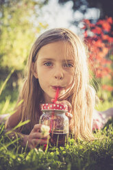 Portrait of little girl lying on a meadow in the garden drinking juice - SARF000728