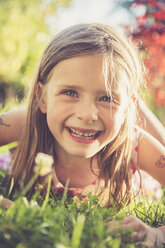Porträt eines lächelnden kleinen Mädchens, das auf einer Wiese im Garten liegt - SARF000729