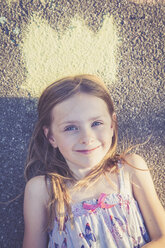 Portrait of smiling little girl lying on tarmac with a painted crown - SARF000730