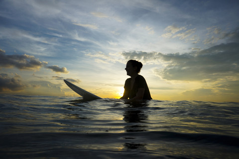 Indonesia, Bali, Canggu, silhouette of young woman with surfboard by twilight stock photo