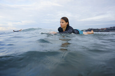 Indonesien, Bali, Canggu, junge Frau auf ihrem Surfbrett liegend in der Vorwärtsbewegung - FAF000053