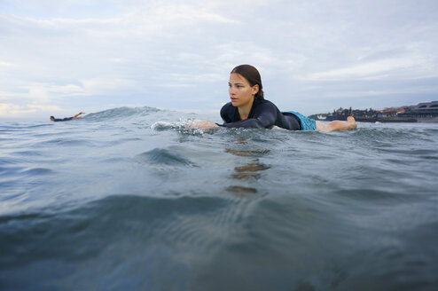 Indonesia, Bali, Canggu, young woman lying on her surf board moving forward - FAF000053