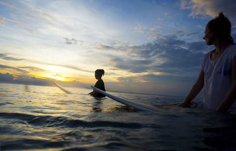 Indonesien, Bali, Canggu, zwei Surferinnen im Wasser, die die Sonne beobachten, lizenzfreies Stockfoto