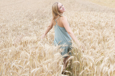 Portrait of smiling young woman with outstretched arms standing in a rye field - DRF000951