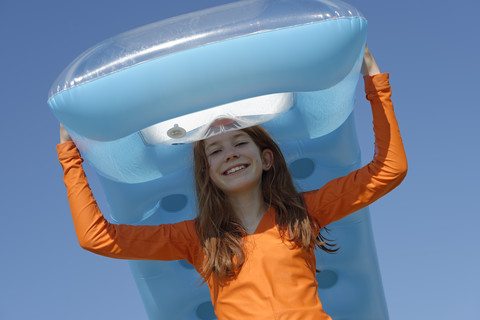 Portrait of smiling girl carrying air mattress on her head wearing sun protection longsleeve stock photo