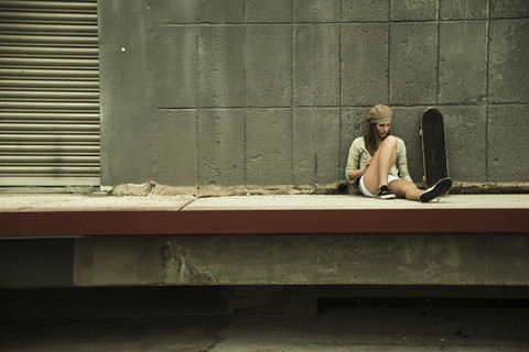 Teenager-Mädchen mit Skateboard an Betonwand, lizenzfreies Stockfoto