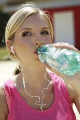 Porträt einer jungen Frau mit Kopfhörern, die Wasser aus einer Flasche trinkt - GDF000359