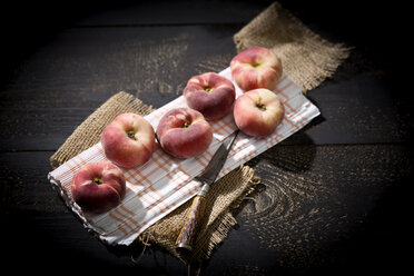 Six doughnut peaches, Prunus persica var. platycarpa, and a knife on cloth and dark wooden table - MAEF008806