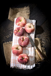 Six doughnut peaches, Prunus persica var. platycarpa, and a knife on cloth and dark wooden table - MAEF008807