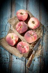 Six doughnut peaches, Prunus persica var. platycarpa, and a knife on cloth and wooden table - MAEF008809