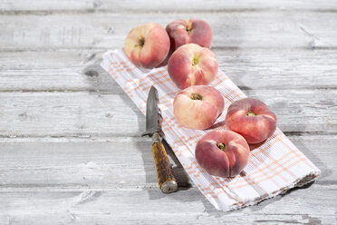 Six doughnut peaches, Prunus persica var. platycarpa, and a knife on cloth and wooden table - MAEF008813