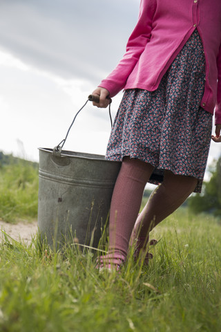 Deutschland, Schleswig-Holstein, kleines Mädchen trägt einen Zinkeimer auf einer Wiese, lizenzfreies Stockfoto