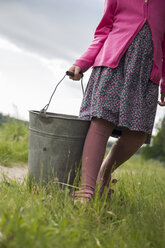 Germany, Schleswig-Holstein, little girl carrying a zinc bucket on a meadow - TKF000374