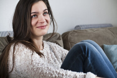 Portrait of smiling young woman sitting on couch in her living room - FEXF000147