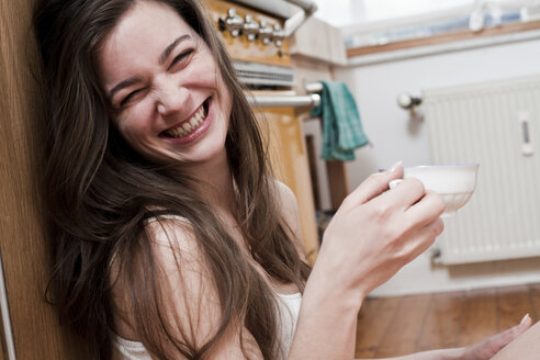 Porträt einer lächelnden jungen Frau mit einer Tasse Tee zu Hause - FEXF000149