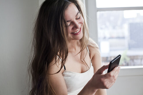 Porträt einer lächelnden jungen Frau, die zu Hause ihr Smartphone benutzt - FEXF000153