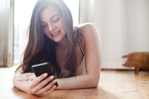 Porträt einer lächelnden jungen Frau, die zu Hause ihr Smartphone benutzt, lizenzfreies Stockfoto