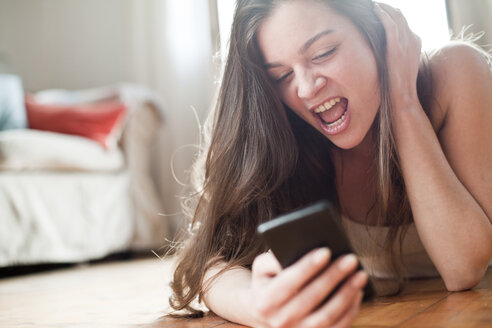 Porträt einer schreienden jungen Frau, die zu Hause ihr Smartphone benutzt - FEXF000154