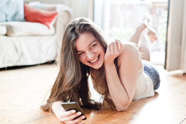 Portrait of smiling young woman with smartphone at her living room - FEXF000155