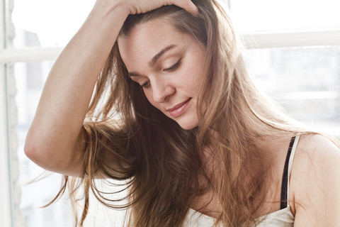 Porträt einer lächelnden jungen Frau mit einer Hand in ihrem Haar, lizenzfreies Stockfoto