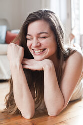 Porträt einer lachenden jungen Frau, die auf dem Boden ihres Wohnzimmers liegt - FEXF000160