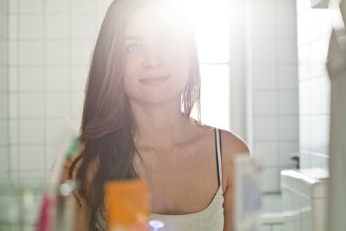 Porträt einer lächelnden jungen Frau, die ihr Spiegelbild im Badezimmer betrachtet - FEXF000166