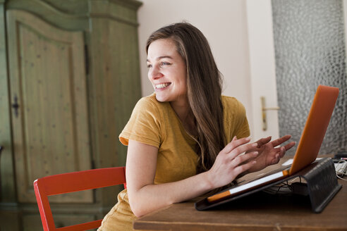 Porträt einer lächelnden jungen Frau mit ihrem Laptop zu Hause - FEXF000228