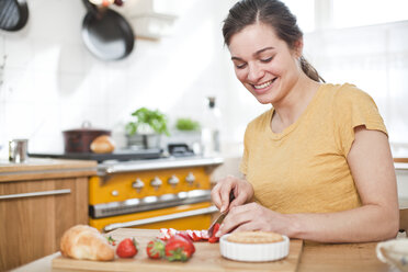 Portrait of smiling young woman cutting strawberries - FEXF000177