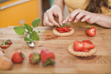 Junge Frau, die Kuchen mit Erdbeeren und Minze garniert, Teilansicht - FEXF000179