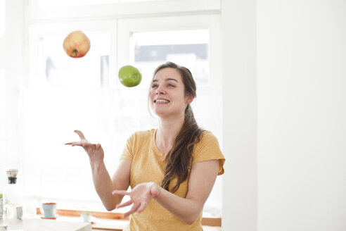 Lächelnde junge Frau jongliert mit zwei Äpfeln in ihrer Küche - FEXF000185
