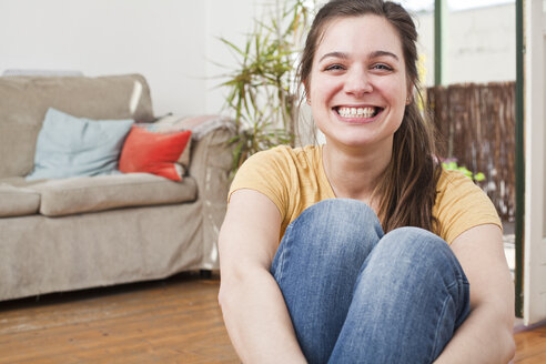Porträt einer grinsenden jungen Frau, die in ihrem Wohnzimmer sitzt - FEXF000198