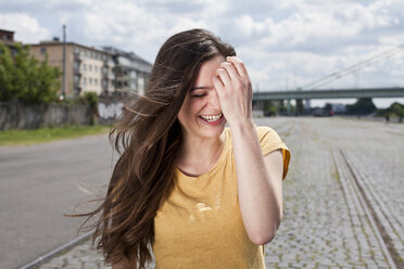 Germany, North Rhine-Westphalia, Cologne, portrait of laughing young woman with hand on her face - FEXF000204