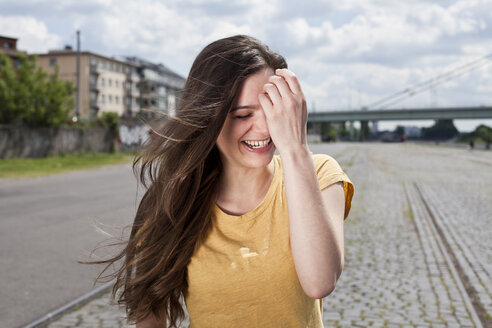 Deutschland, Nordrhein-Westfalen, Köln, Porträt einer lachenden jungen Frau mit Hand im Gesicht - FEXF000204