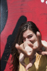 Portrait of smiling young woman showing victory-sign in front of a graffiti - FEXF000207