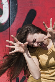 Porträt einer jungen Frau, die ein Gesicht vor einem Graffiti macht - FEXF000208
