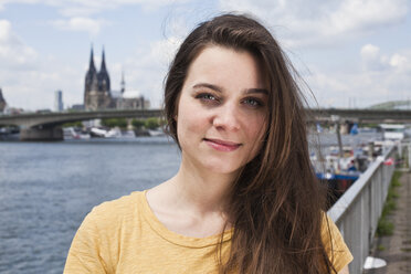 Germany, Cologne, portrait of smiling young woman standing in front of Rhine River - FEXF000210