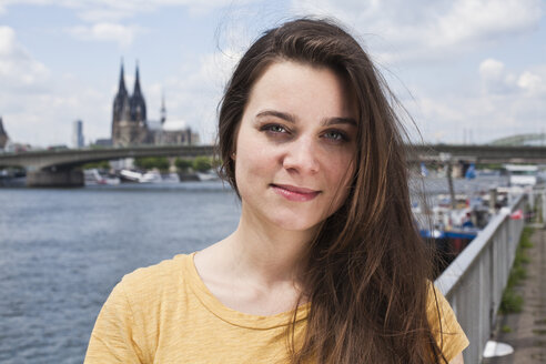 Deutschland, Köln, Porträt einer lächelnden jungen Frau, die vor dem Rhein steht - FEXF000210