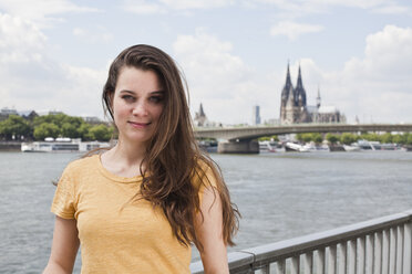 Germany, Cologne, portrait of smiling young woman standing in front of Rhine Rive - FEXF000211