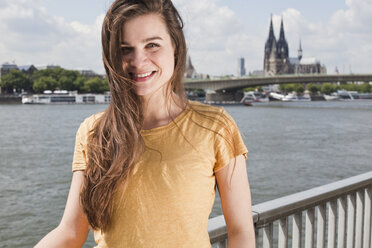 Germany, North Rhine-Westphalia, Cologne, portrait of smiling young woman in front of Rhine River - FEXF000212